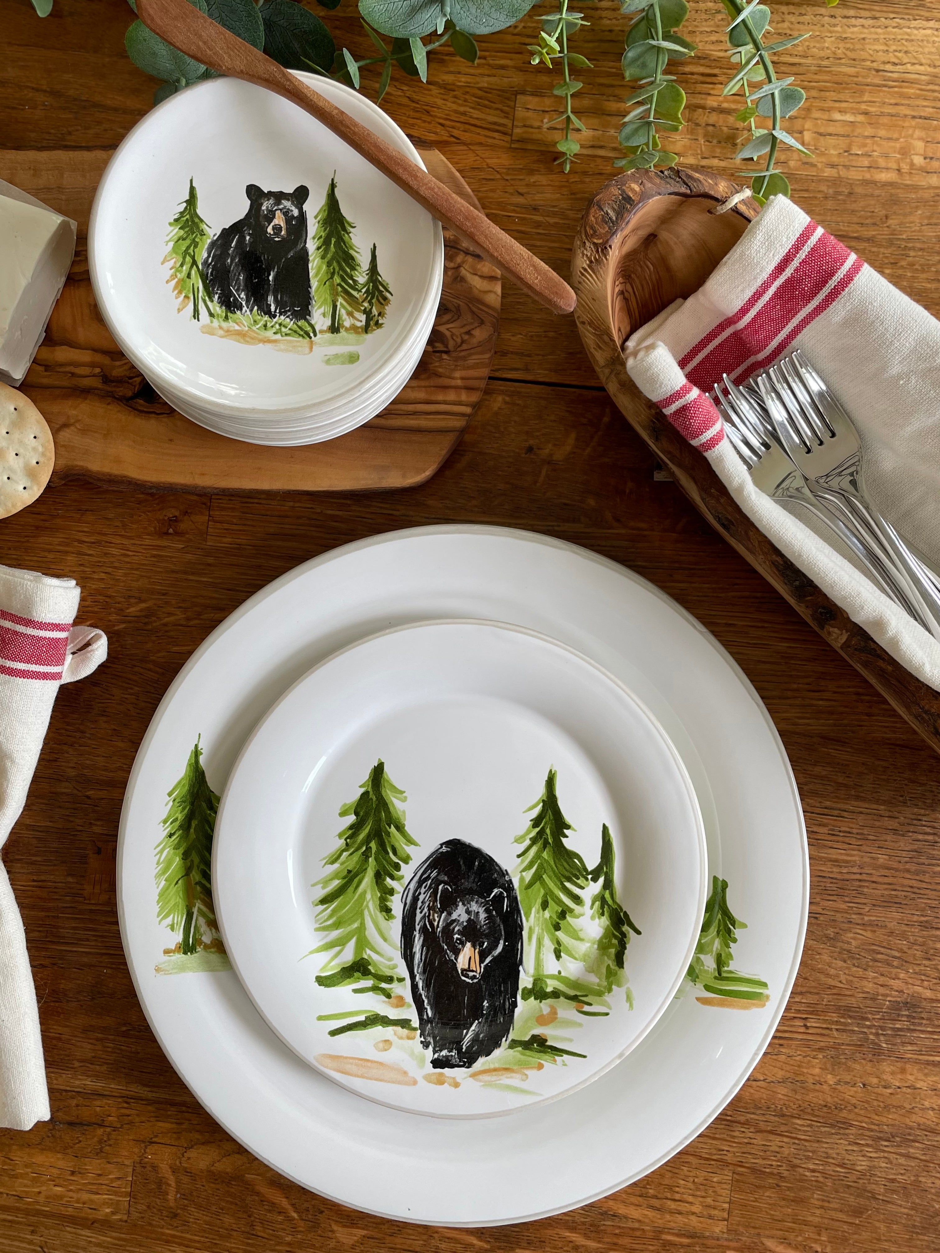 White plates with black bear and green tree design on a wooden table.